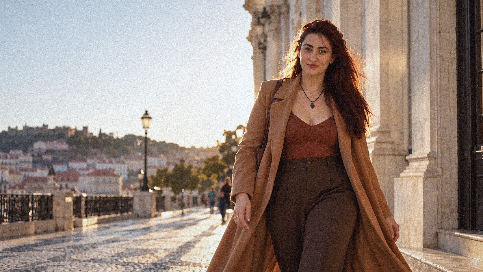 Rachel Cossich caminhando numa rua de Lisboa ao fim da tarde, de casaco longo camel