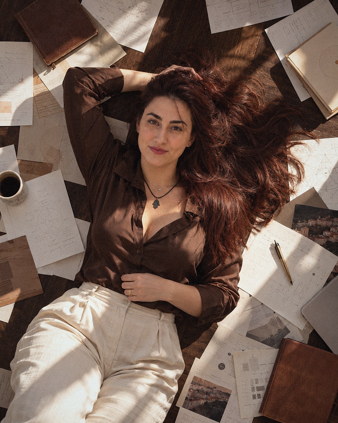 Rachel deitada no chão de madeira, cercada de mapas e anotações