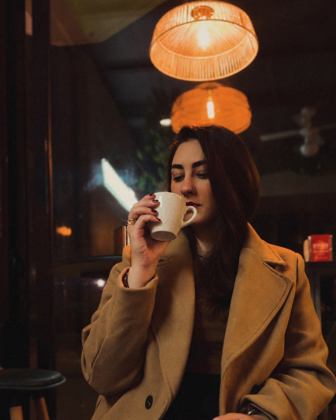 Rachel tomando um café num café de Lisboa, de casaco camel